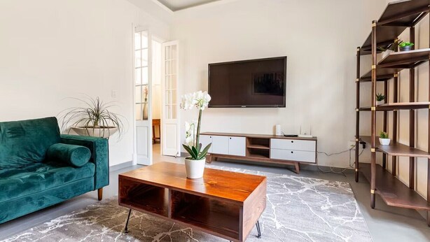 A modern living room with a teal sofa, a wooden coffee table, a TV, and a bookshelf. - Amazing Apartment in Condesa (Ciudad de México)