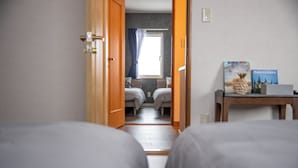 Camera d'albergo con due letti, una finestra con tende, un tavolino con un libro e un interruttore della luce fissato al muro.