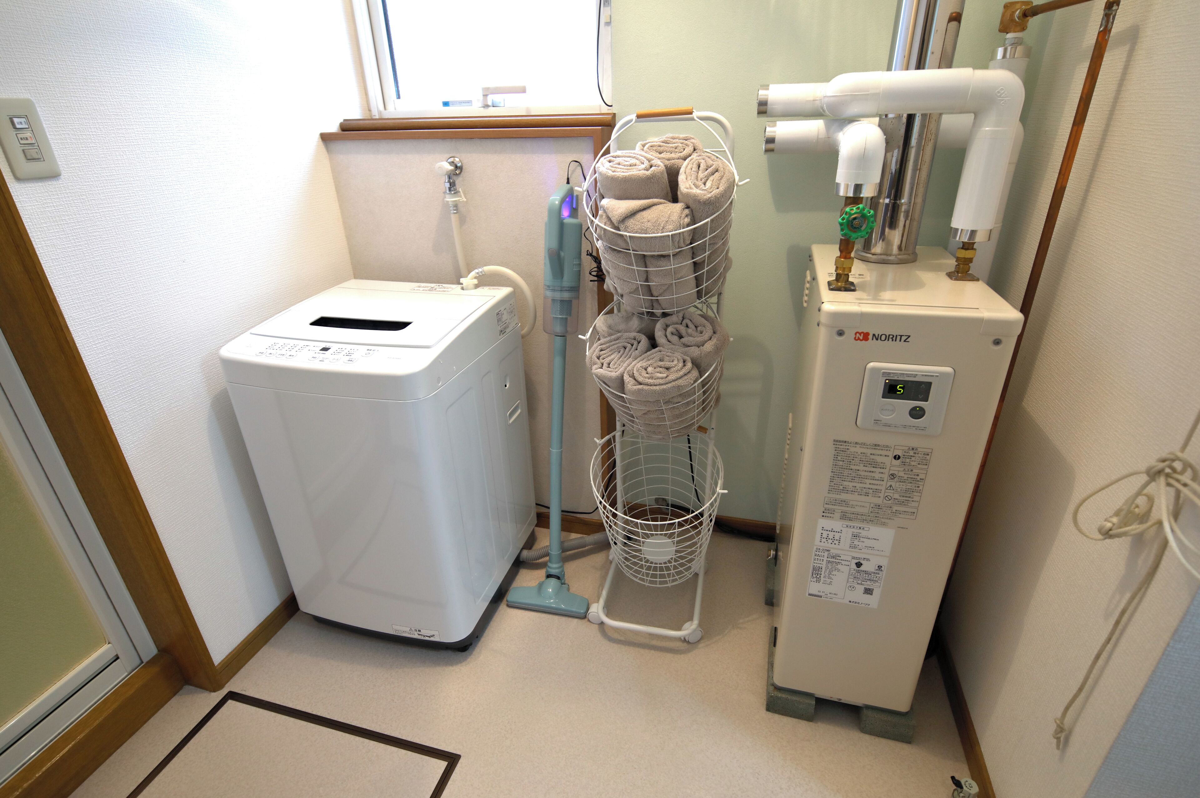A laundry room with a front-loading washing machine, a stacked towel rack, and a water heater.