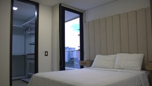 A bedroom with a bed, a nightstand, a closet, and a window with a view of buildings. - 1002 - Beautiful Apartment In El Poblado Medellin (Medellín)
