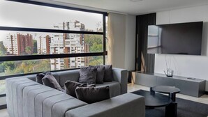 A modern living room with a grey sectional sofa, a coffee table, and a flat-screen TV mounted on the wall. - 1002 - Beautiful Apartment In El Poblado Medellin (Medellín)