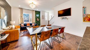 Un salon moderne comprenant un coin repas, un lustre, un téléviseur à écran plat et un mur décoré dans des tons verts.