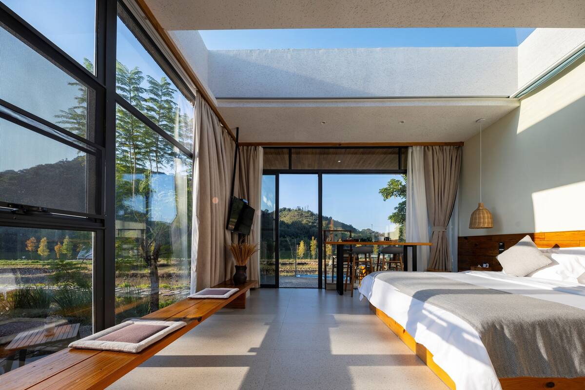 Ein modernes Schlafzimmer mit einem großen Bett, einem Schreibtisch und Blick auf eine Berglandschaft durch große Fenster.