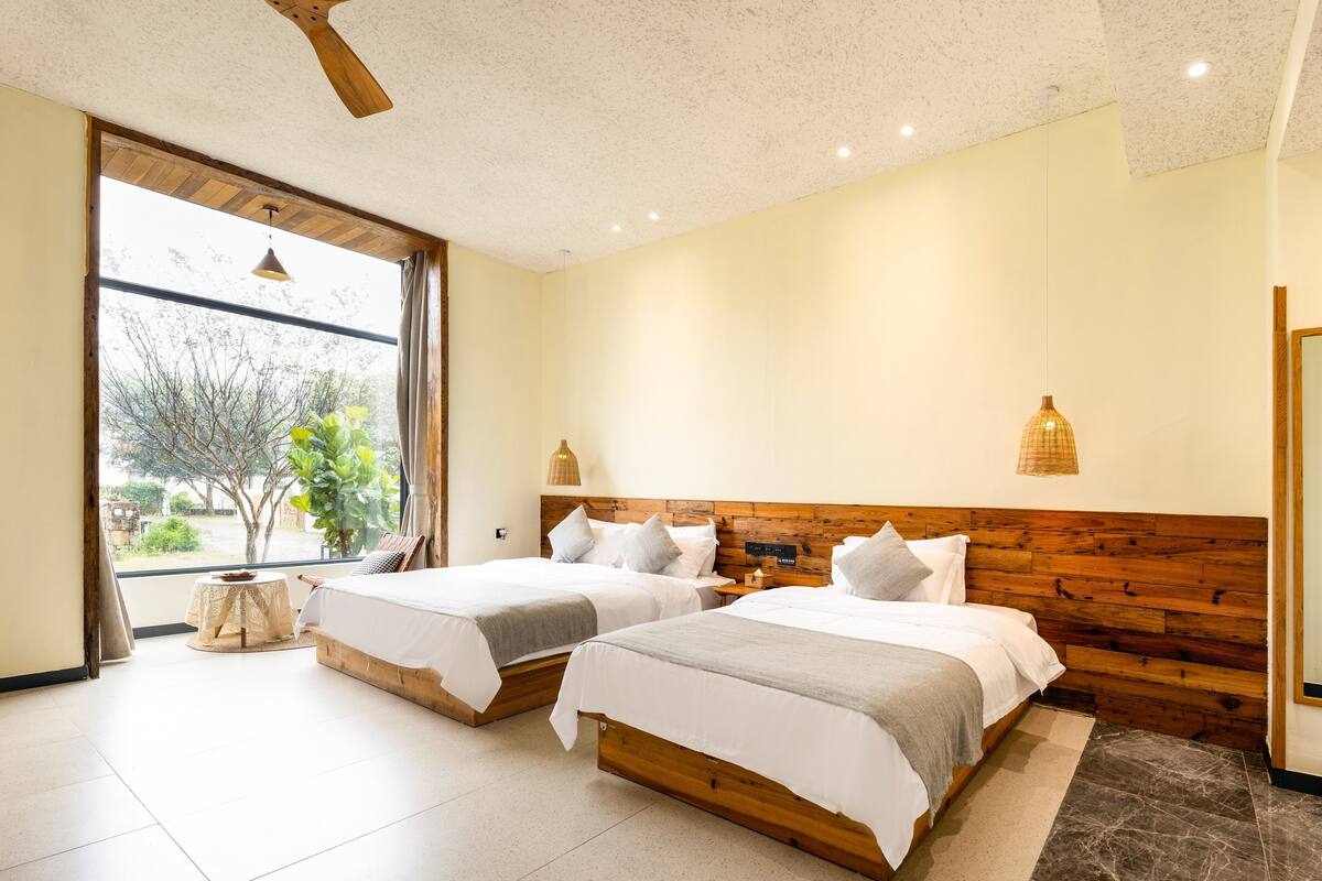 Ein modernes Schlafzimmer mit zwei Betten, einem Holzkopfstück, einem Deckenventilator und Blick ins Freie.
