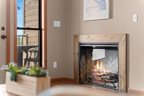 Une cheminée avec une façade en verre, une cheminée en bois et un feu qui crépite à l’intérieur.
