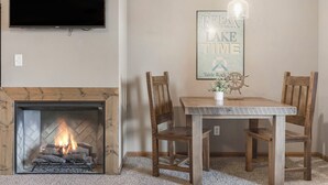 A living room with a fireplace, a dining table with two chairs, a television mounted on the wall, and a pendant light above the table. - 2BD, Sleeps 8 Lake Condo, Resort Perks, Ticket/Golf Deals (Branson)