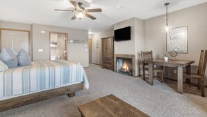 A bedroom with a bed, a ceiling fan, a fireplace, a dining table, and a TV mounted on the wall. - 2BD, Sleeps 8 Lake Condo, Resort Perks, Ticket/Golf Deals (Branson)