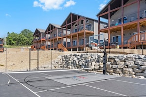 A multi-story residential building with balconies, a basketball court, and a stone wall.