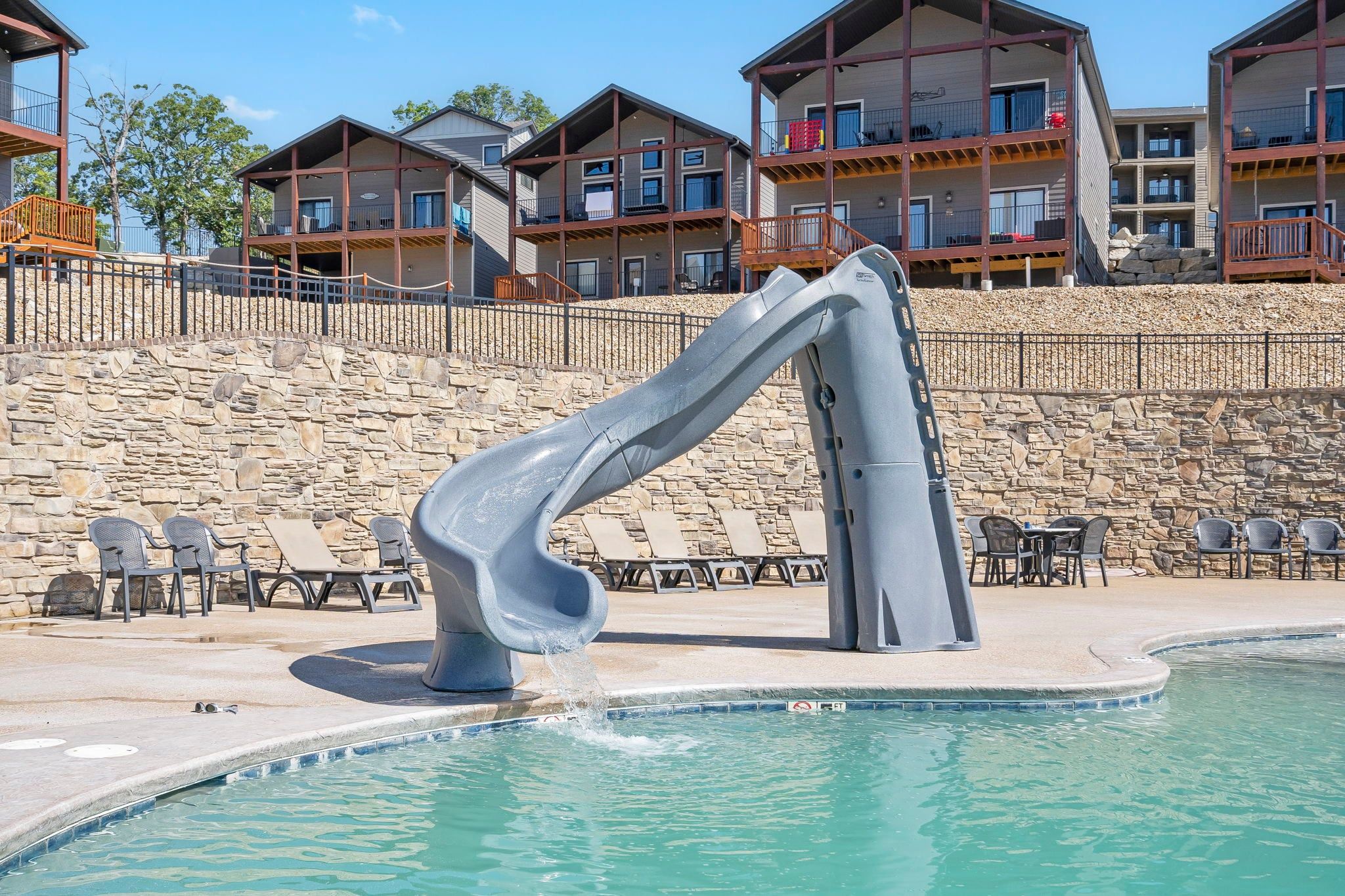 A swimming pool with a slide, lounge chairs, and a stone wall.