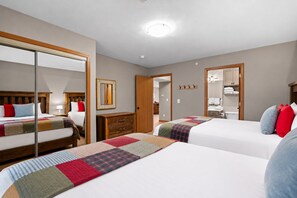 Une chambre d’hôtel avec deux lits, une armoire, un miroir et une salle de bain visible à travers une porte ouverte.