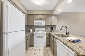 A kitchen with beige cabinets, a white stove, a microwave, and a granite countertop.