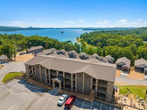 A multi-story hotel with a parking lot, surrounded by lush greenery and a lake view.