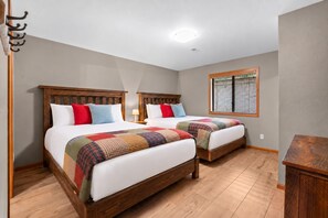 Ein Schlafzimmer mit zwei Betten, Holz-Kopfteilen, einem Fenster mit Jalousien und einem Nachttisch aus Holz.