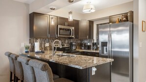A modern kitchen with dark cabinetry, stainless steel appliances, a granite countertop, and bar stools. - 2 BD Lake View Condo, with Jacuzzi Tub, Covered Deck, Resort Amenities and Discount Tickets (Branson)