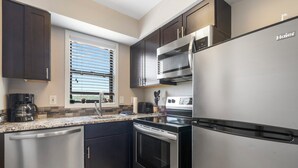 A modern kitchen with dark cabinets, stainless steel appliances, a window with blinds, and a countertop with a coffee maker. - Beautiful Lake View 1 BD with Jacuzzi Tub and Free Resort Amenities, Ticket Discounts! (Branson)