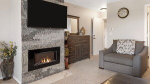 A living room with a stone fireplace, a flat-screen TV, a sofa, and a decorative vase. - Beautiful Lake View 1 BD with Jacuzzi Tub and Free Resort Amenities, Ticket Discounts! (Branson)