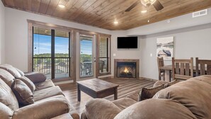 A cozy living room with a fireplace, wooden ceiling, and large windows.