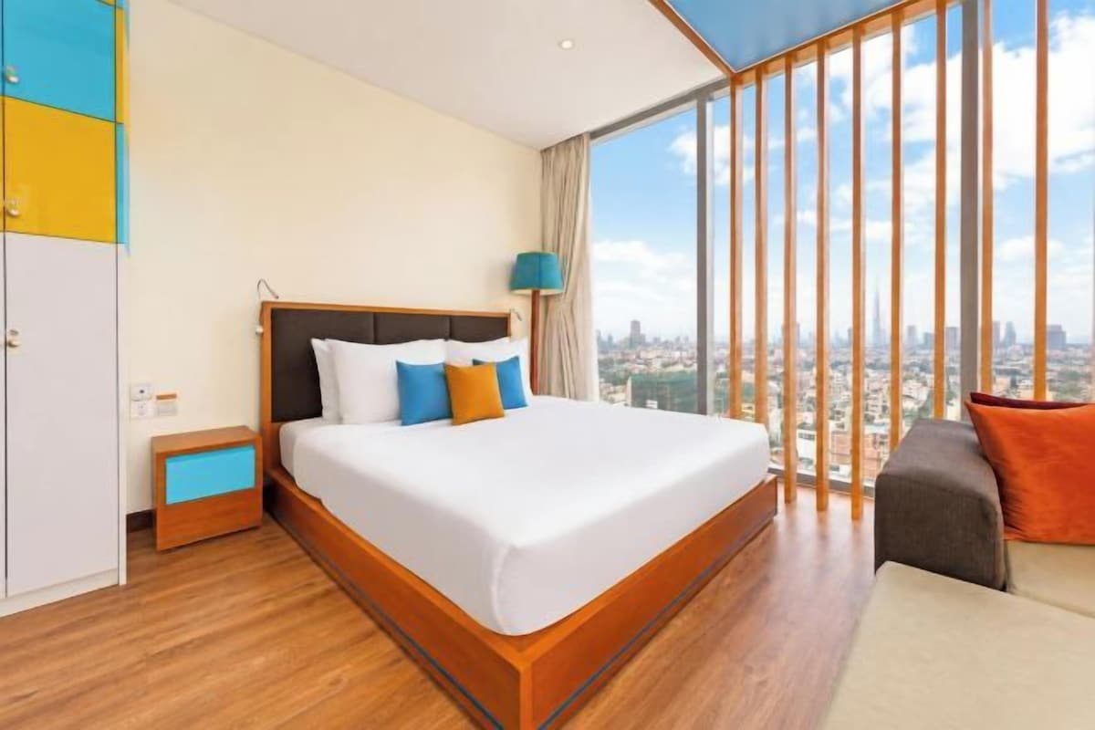 A hotel room with a large bed, a view of the city, and a balcony with a cityscape view.