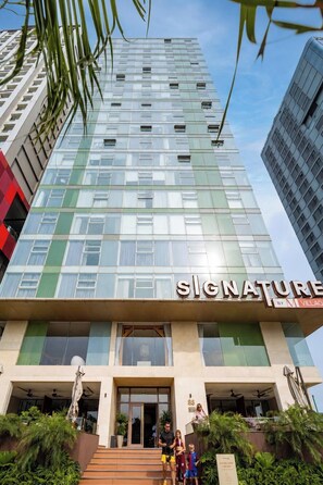 Un bâtiment moderne à la façade vitrée, sur lequel on peut voir un grand panneau indiquant le nom « SIGNATURE », et un escalier menant à l’entrée.