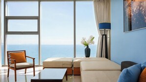 A modern living room with a view of the sea, a sofa, a chair, a coffee table, and a floor lamp. - Sea and Sun Apartments (Da Nang)