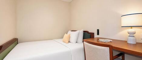 A hotel room with a single bed, a bedside table, a chair, and a desk with a lamp.