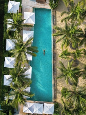 A rectangular swimming pool with a person in the center, surrounded by white umbrellas and palm trees. - Sea and Sun Apartments (Da Nang)