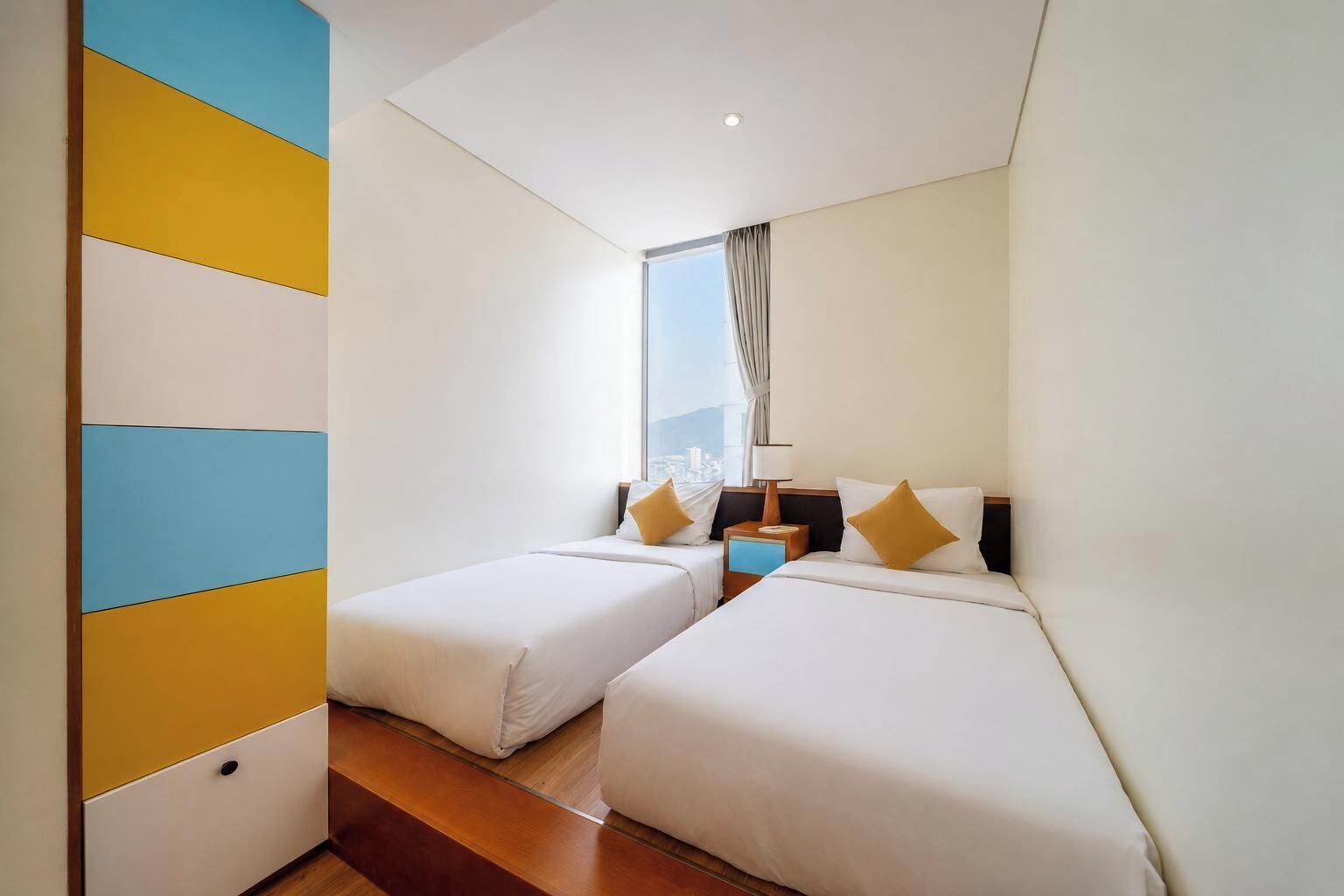 A hotel room with two beds, a window with curtains, a nightstand, and a view of the city.