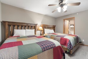 A bedroom with two beds, wooden headboards, a ceiling fan, and a nightstand with a lamp.