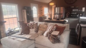 Una sala de estar acogedora con un sofá seccional, un perro y una zona de cocina con refrigerador y microondas.