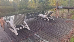 Una terraza de madera con dos sillas reclinables que dan a un cuerpo de agua, rodeada de árboles.