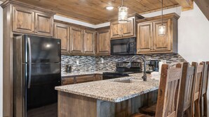 A kitchen with wooden cabinets, a stainless steel refrigerator, a microwave, and a granite countertop. - Sweet 3BR + Loft With Spectacular View of Lake (Branson)