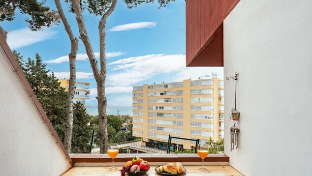 Un balcon avec une table dressée pour deux personnes, agrémentée d’un panier de fruits, de croissants et de deux verres de jus d’orange.
