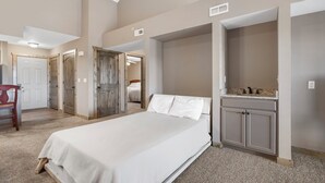 A bedroom with a large bed, a wooden door, a small bathroom with a sink, and a carpeted floor. - Penthouse Condo + Suite, Gorgeous View of the Lake (Branson)