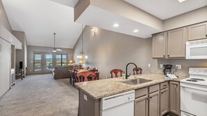 A modern kitchen with granite countertops, a dishwasher, and a stove. There is a dining area with a table and chairs in the background. - Penthouse Condo + Suite, Gorgeous View of the Lake (Branson)
