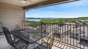 A balcony with a table and chairs, a ceiling fan, and a view of a lake and houses. - Penthouse Condo + Suite, Gorgeous View of the Lake (Branson)