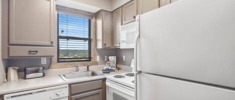 A kitchen with a dishwasher, oven, refrigerator, and a window with blinds.