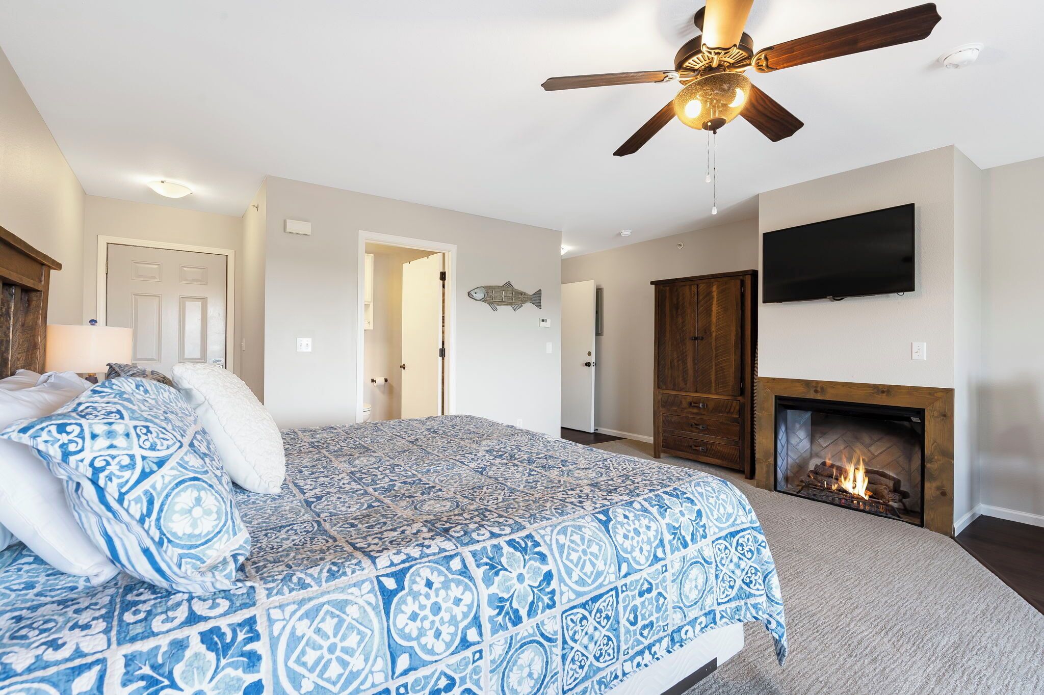 A bedroom with a bed, a ceiling fan, a fireplace, and a television on the wall.