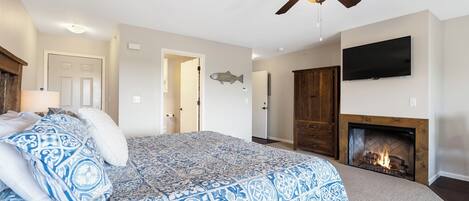 A bedroom with a bed, a ceiling fan, a fireplace, and a television on the wall.