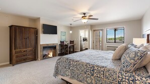 A bedroom with a large bed, a ceiling fan, a fireplace, and a view of the outdoors. - Gorgeous, Unique Connecting Condo and King Suite with Lake View (Branson)