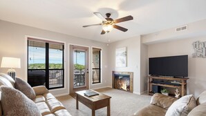 A living room with a sofa, a coffee table, a fireplace, a TV, and a ceiling fan. - Gorgeous, Unique Connecting Condo and King Suite with Lake View (Branson)