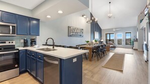 A modern kitchen with blue cabinets, a central island, and a dining area with a view.