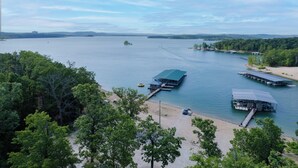 A lakeside property with docked boats, a covered boat launch, and a parking area surrounded by trees.