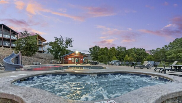 Ein Whirlpoolbereich mit einer Holzhütte im Hintergrund, umgeben von Liegestühlen und einem Pool.