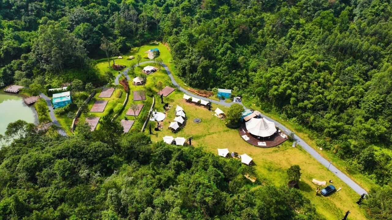 Vista aérea de un camping con tiendas de campaña y una estructura circular central, rodeado de un bosque denso.