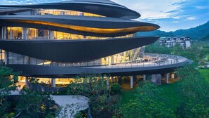 Un edificio moderno de varios niveles con un diseño curvo singular, que cuenta con terrazas exteriores y una cascada.