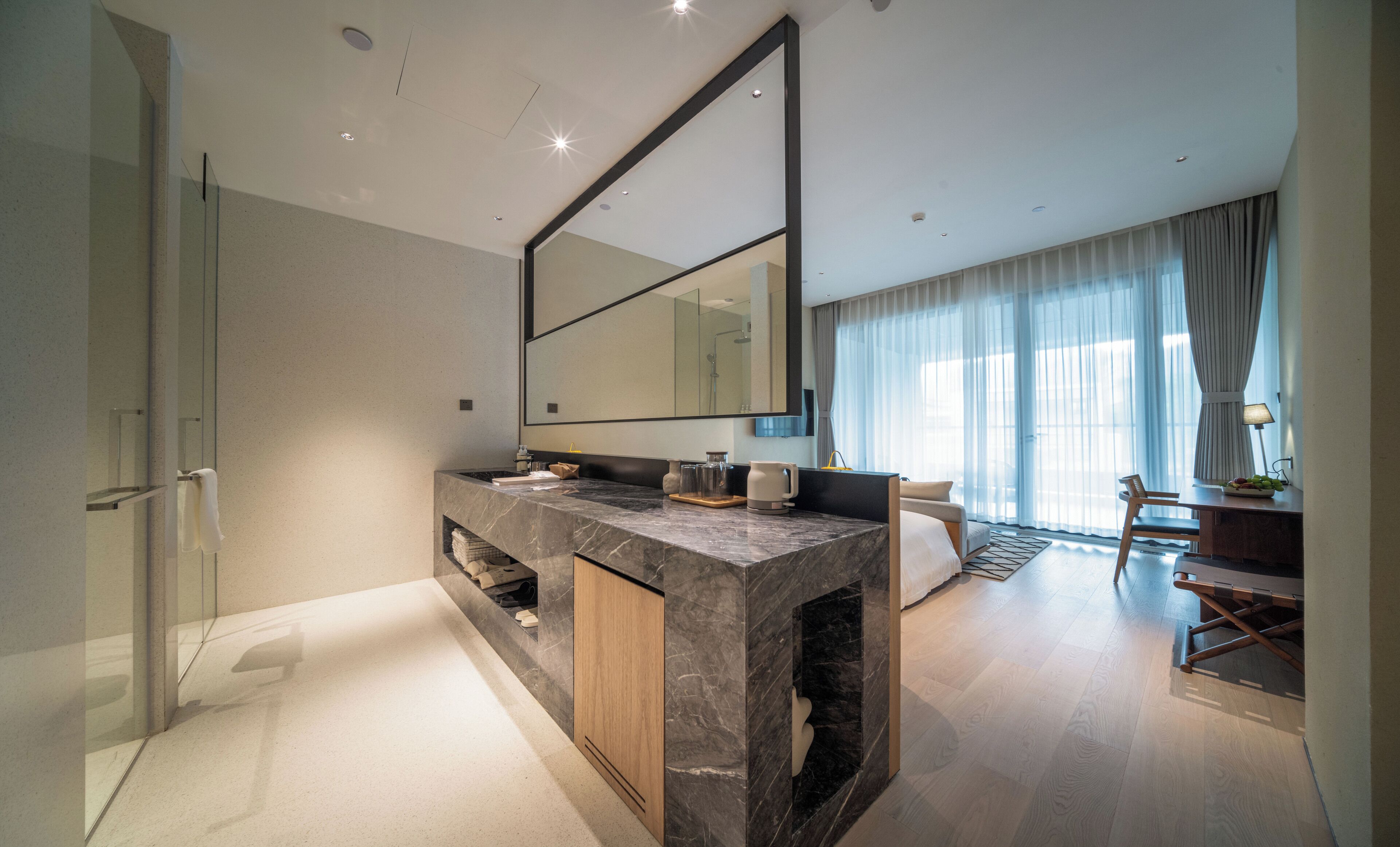 Un baño moderno con un espejo grande, encimera de mármol y zona de ducha.