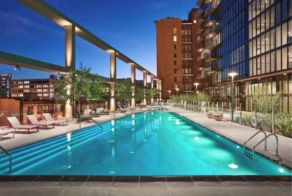 A swimming pool with lounge chairs and a modern building in the background.