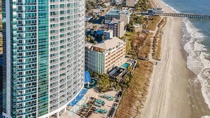 A high-rise hotel with multiple floors, a beachside location, and a pier extending into the ocean. - Wake up to sweeping ocean views from the 16th floor at Oceans One (Myrtle Beach)