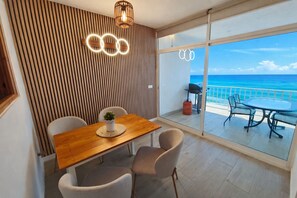 A dining area with a wooden table and chairs, a potted plant, and a view of the ocean through large glass doors. - Exclusive Sea View Apartment EHHouse (Buenas Noches)