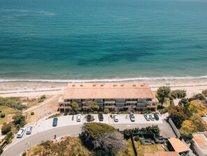 An aerial view of a coastal building with a parking lot, adjacent to a beach and the sea. - Exclusive Sea View Apartment EHHouse (Buenas Noches)